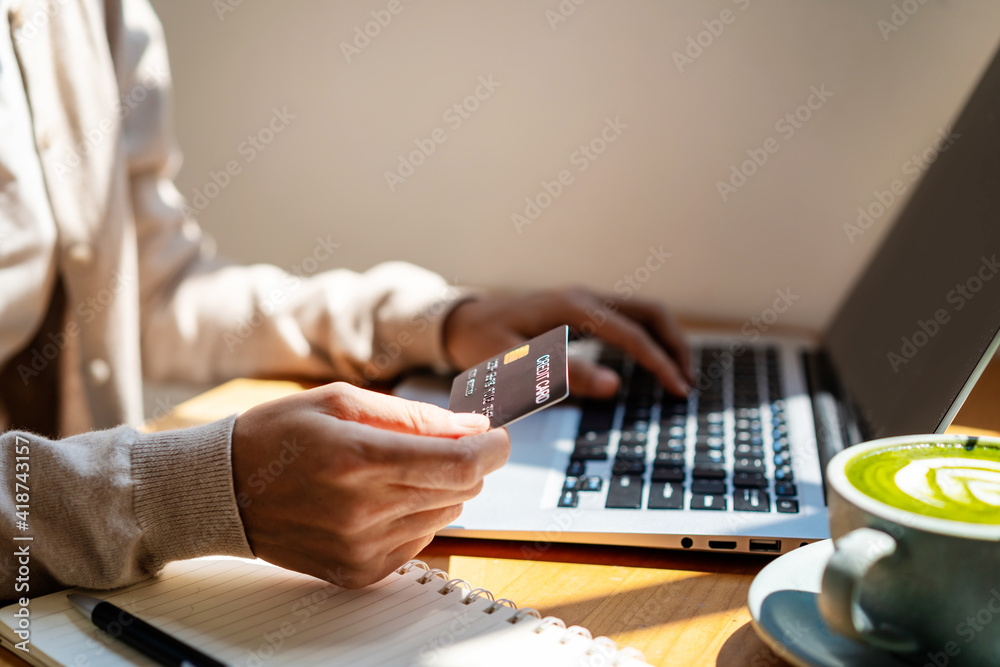 年轻女子持有信用卡，在咖啡店使用电脑进行在线支付购物