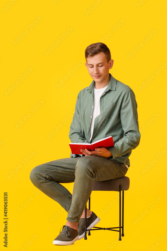 年轻人坐在彩色背景的扶手椅上阅读红色书籍