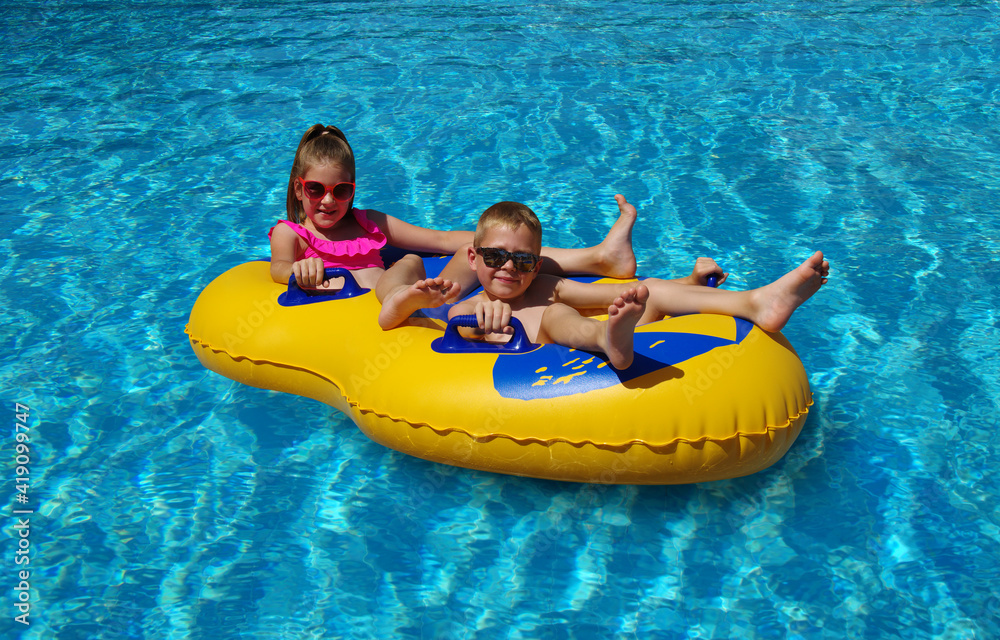 室外游泳池里，男孩和女孩在充气浮漂上。
