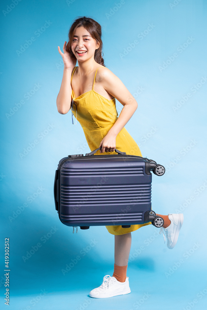 亚洲年轻女性拿着蓝色背景的行李箱，夏天的概念