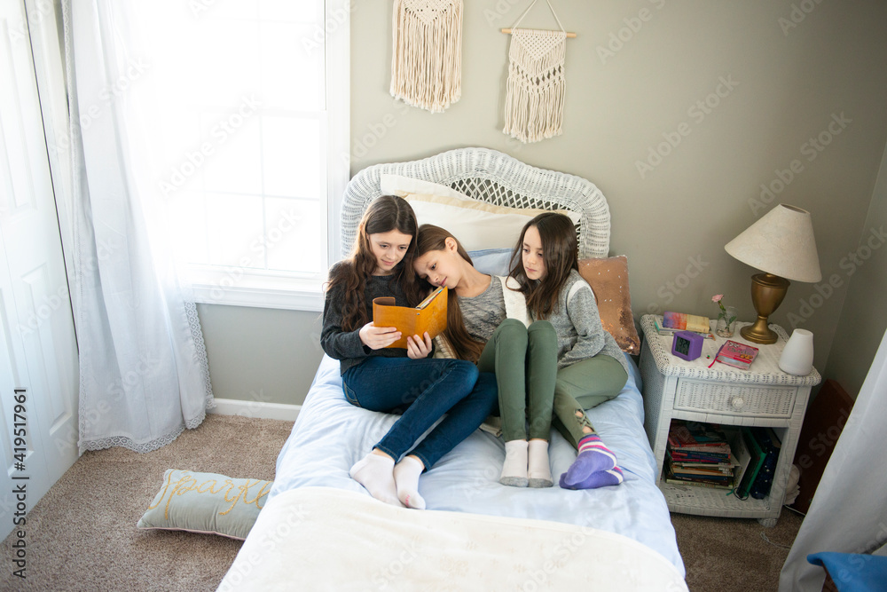 三姐妹在阳光充足的卧室里一起在床上看书。
