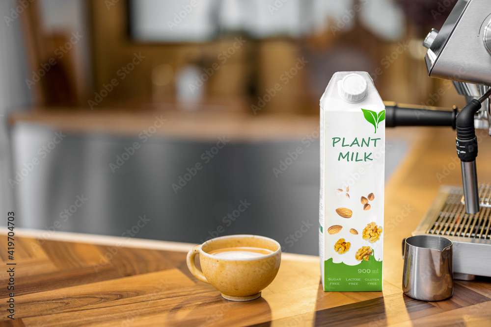 在木制桌面上的一杯咖啡、钳子和咖啡机附近包装植物奶