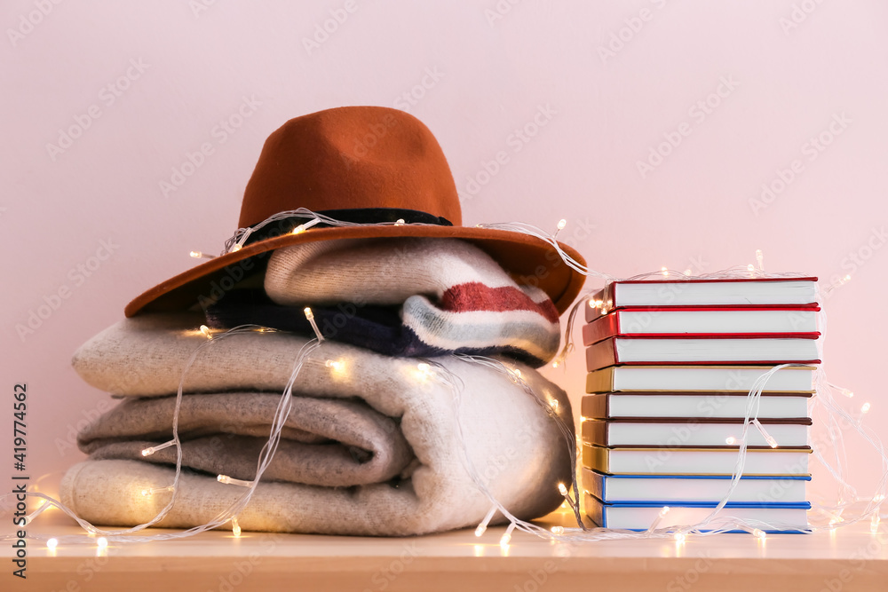 一摞书，时尚的帽子和格子布放在桌子上，靠着彩色墙