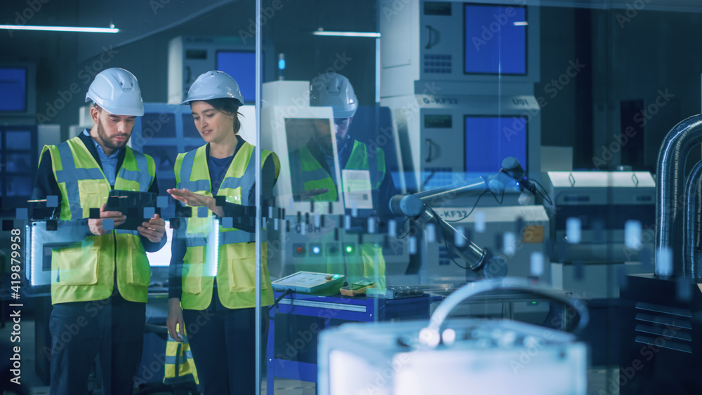 现代工厂：女性和男性工程师穿着安全夹克，戴着安全帽站在工业区