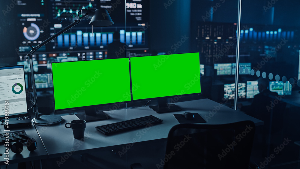 现代监控办公室中的两个数字计算机屏幕和一个绿色实体Chromacey。控制室