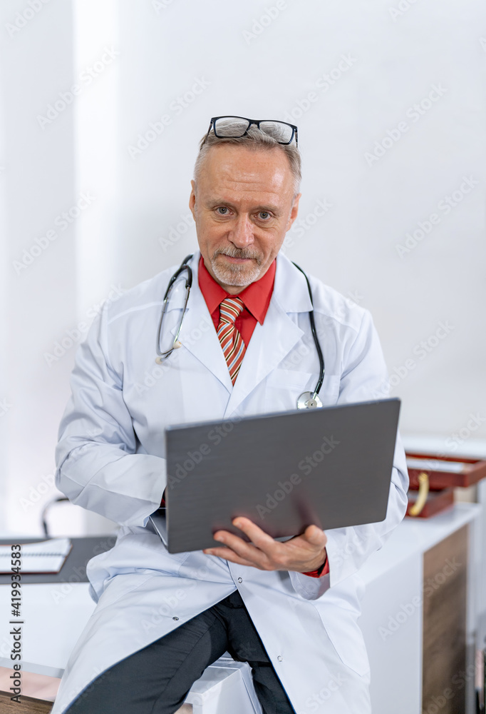 医务室里带着笔记本电脑微笑的资深男医生。医学、专业、技术和人