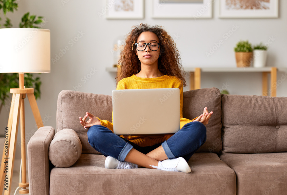Young mixed race woman meditating with closed eyes while working or studying online in living room a