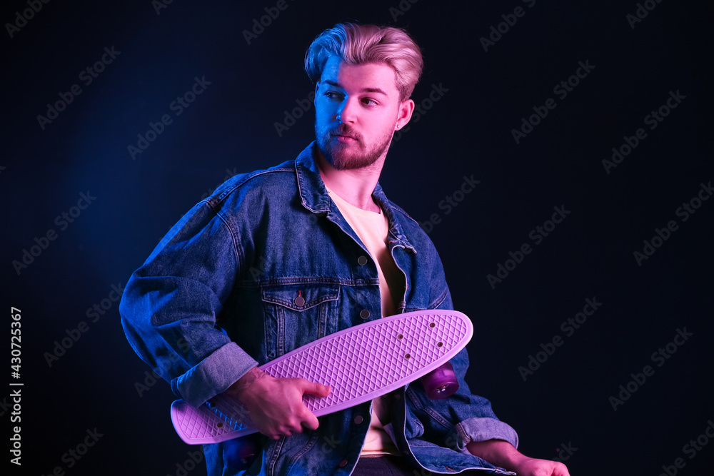Toned portrait of handsome young man with skateboard on dark background