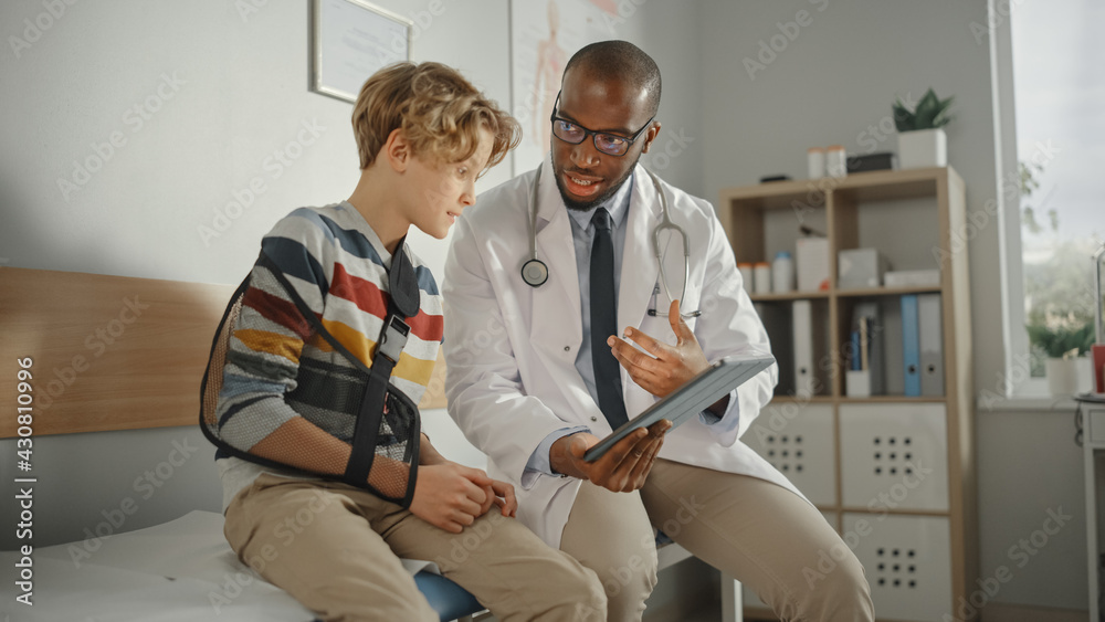 Friendly African American Family Doctor Talking with a Young Boy with Arm Brace and Showing Test Res