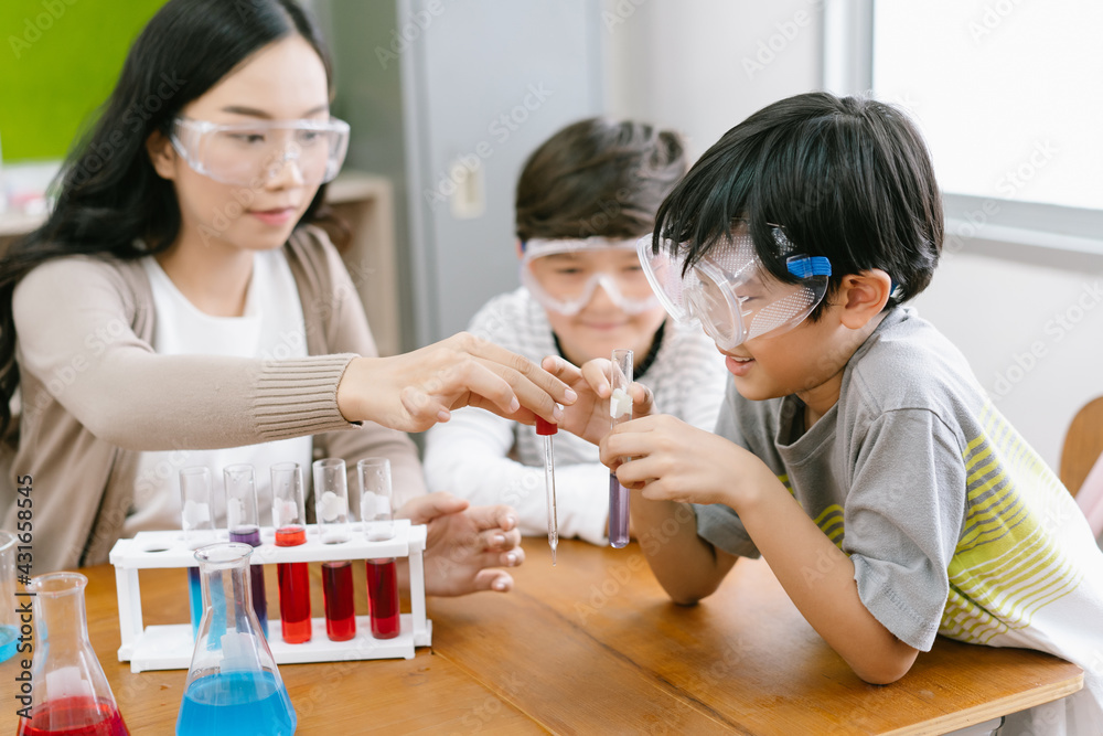 Cute Asian elementary schoolboy doing science while classmates looking his in science class with you