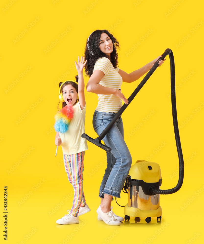 Mother and daughter with vacuum cleaner on color background