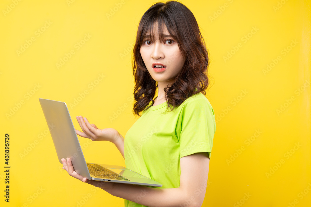 年轻的亚洲女孩在黄色背景下使用笔记本电脑