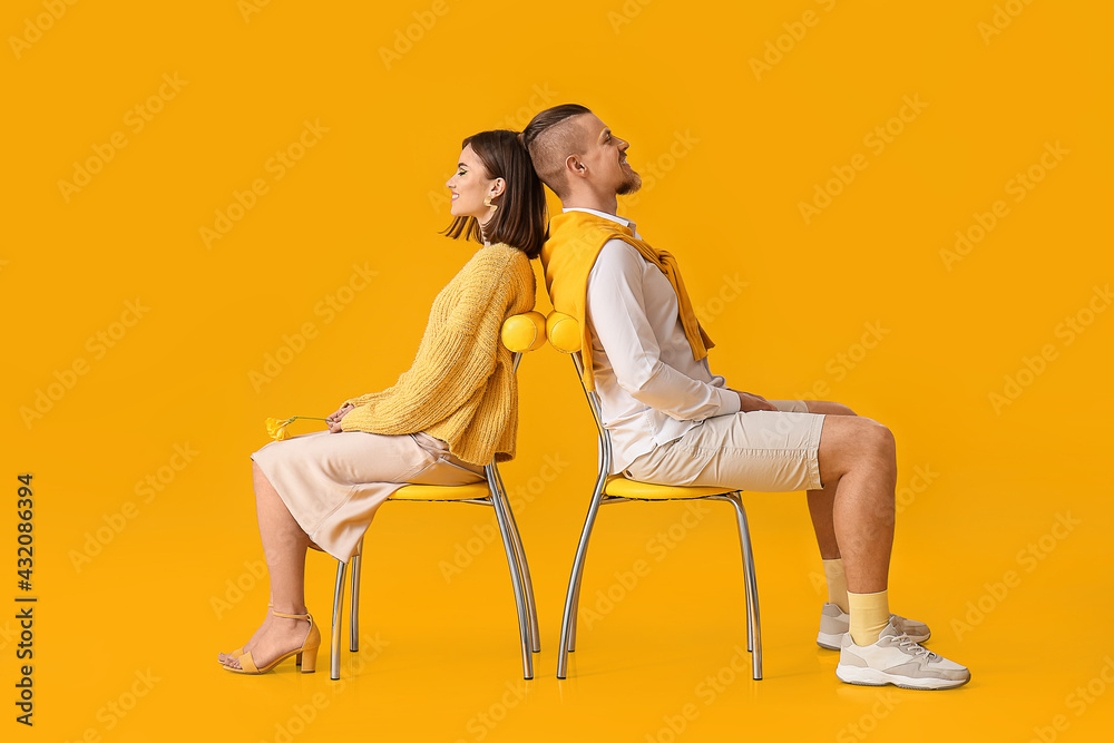 幸福的年轻情侣坐在黄色背景的椅子上
