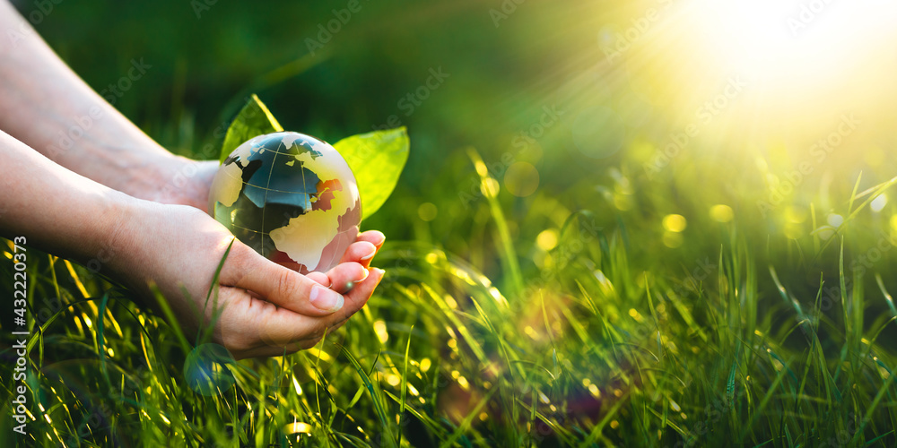 在阳光明媚的绿草中手持水晶地球仪。环境，拯救清洁地球，生态康