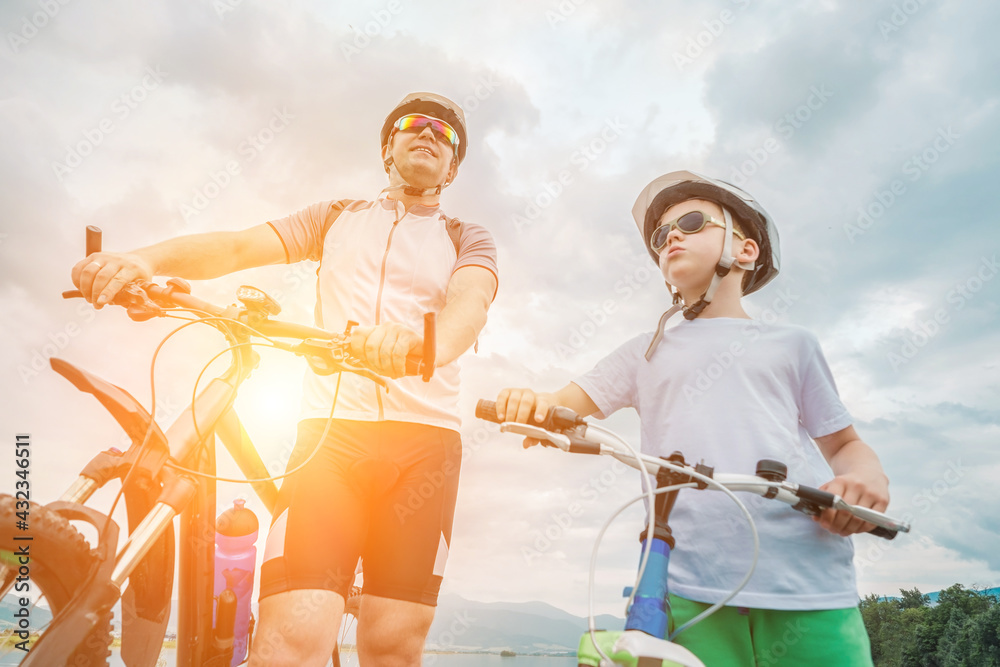 父亲和儿子一起骑行，在阳光明媚的日子里，戴着头盔的幸福家庭正在骑行b