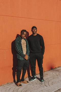 Vertical shot of two Black men standing against a red wall