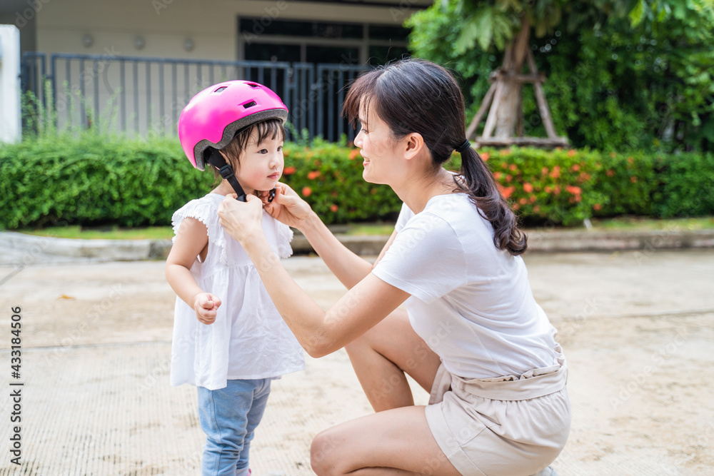 亚洲母亲在骑自行车前给女儿戴上安全帽。