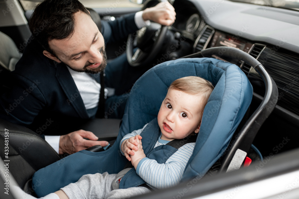 Father tend a child while driving at work with baby sitting in modern car seat. Child new born trave