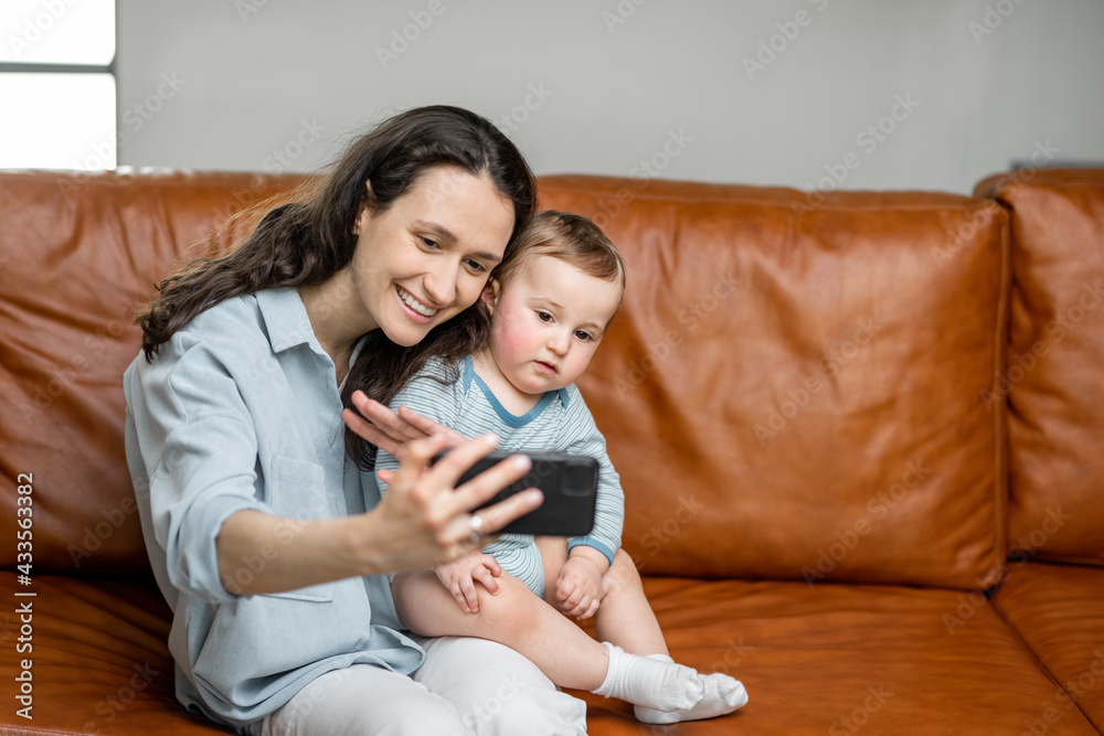 年轻的妈妈和刚出生的儿子坐在沙发上，打视频电话或和婴儿自拍。输入