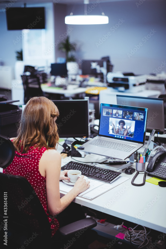 高加索女商人坐在办公桌前，用笔记本电脑与一群同事进行视频通话