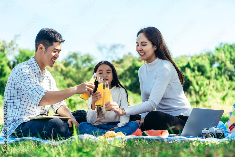 快乐的亚洲家庭正在花园里野餐，和女儿一起喝瓶装橙汁