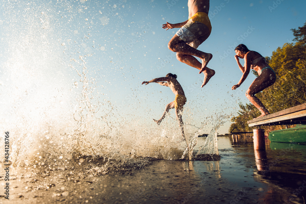 Friends having fun enjoying a summer day swimming and jumping at the lake.