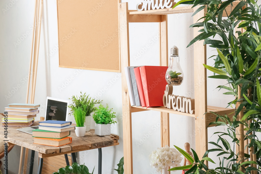 Comfortable workplace with shelf unit, books and houseplants in interior of room