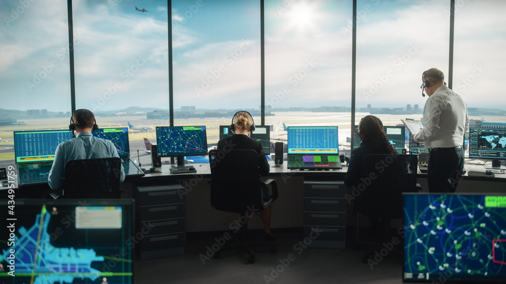 多样化的空中交通管制团队在现代机场塔台工作。办公室里摆满了桌面C