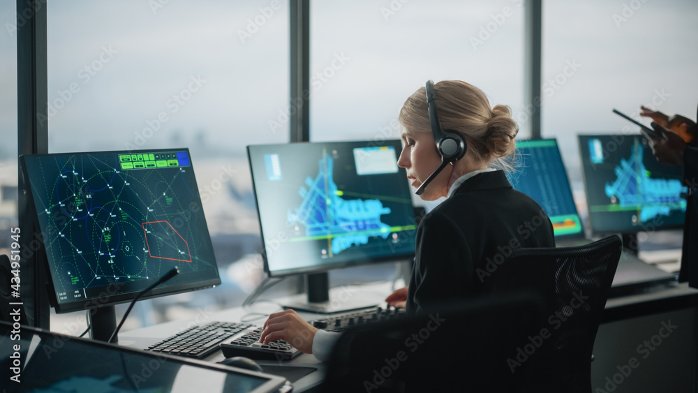 Female Air Traffic Controller with Headset Talk on a Call in Airport Tower. Office Room is Full of D