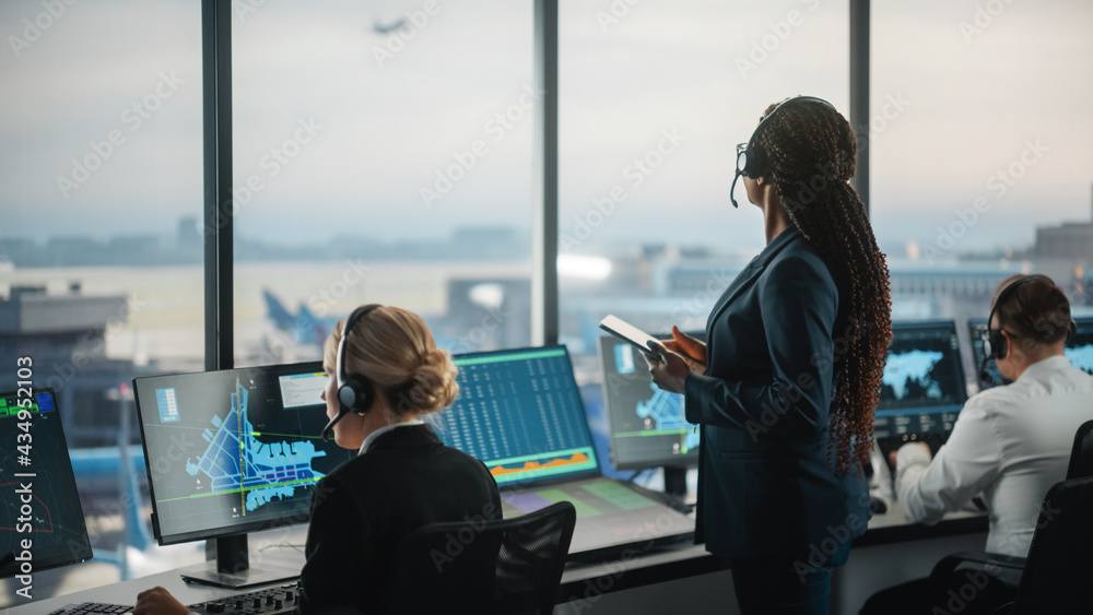 机场塔台黑人女空中交通管制员手持平板电脑。办公室里摆满了桌面