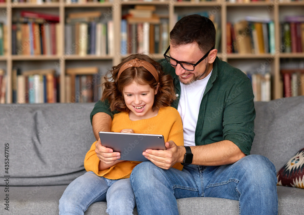 年轻的父女在家里一起看数字平板电脑上的视频