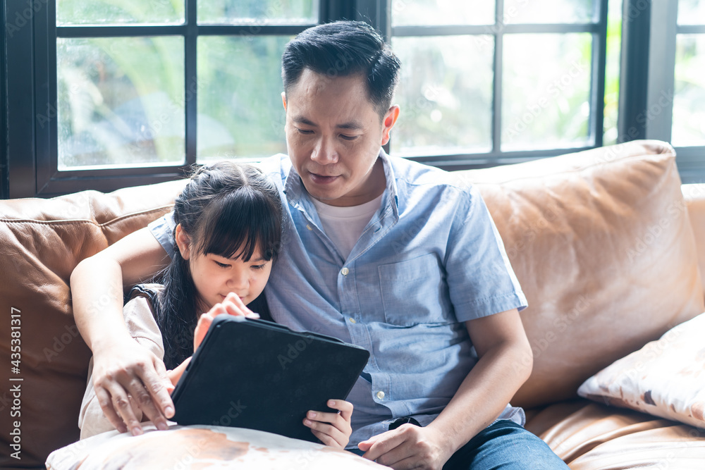 亚洲在家上学的女孩使用平板电脑在线学习，与父亲坐在一起