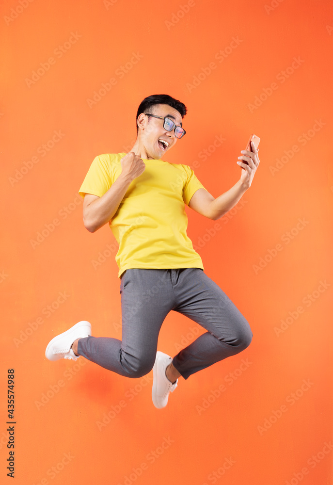 Asian man in yellow t-shirt jumping on orange background