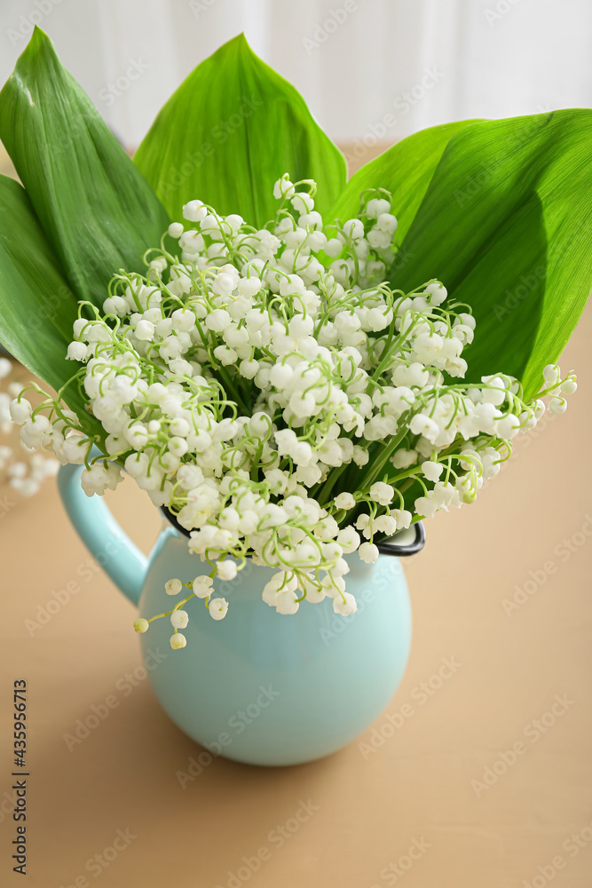 Jug with beautiful lily-of-the-valley flowers on color table