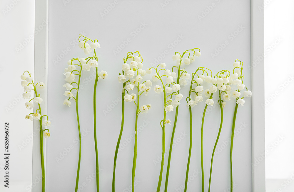 Photo frame with beautiful lily-of-the-valley flowers on light background