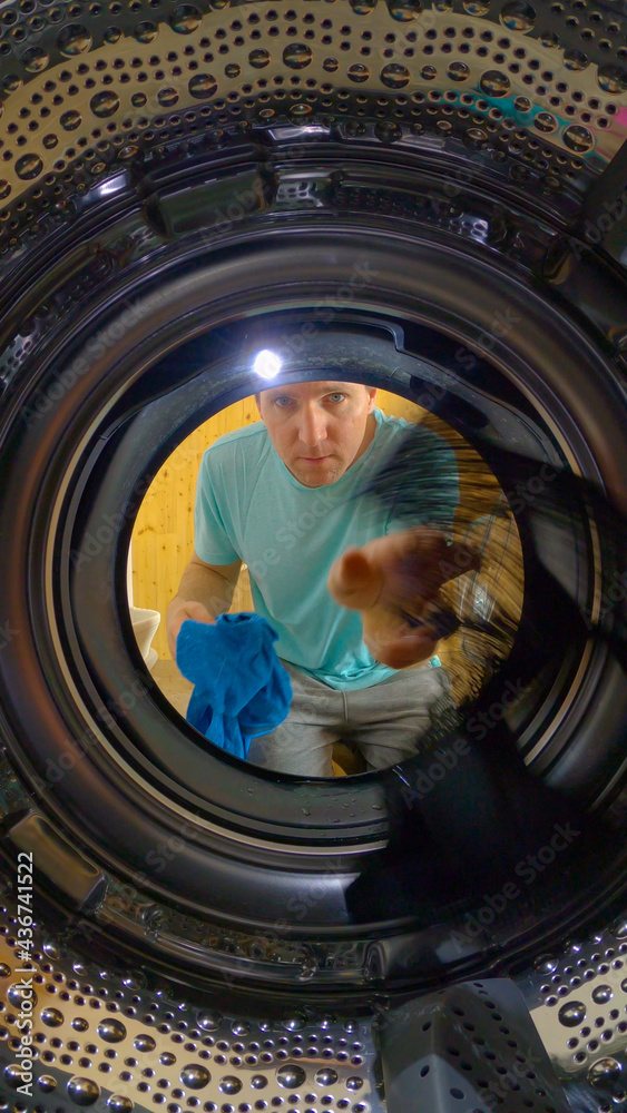 垂直，肖像：一个年轻的高加索男子把脏衣服装进洗衣机。