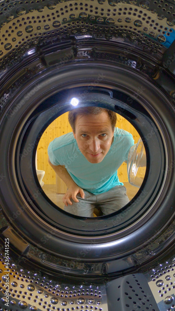 垂直：微笑的男人打开门，看着空荡荡的洗衣机。