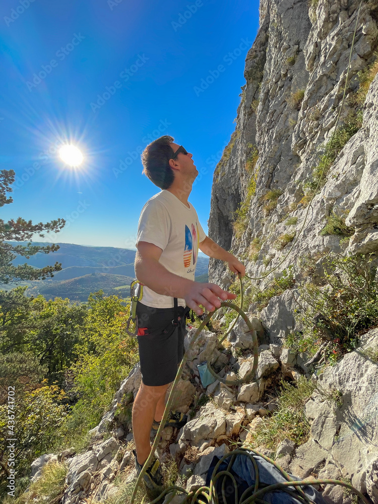 VERTICAL: Man looks up the rocky cliff while rock climbing in sunny Crni Kal