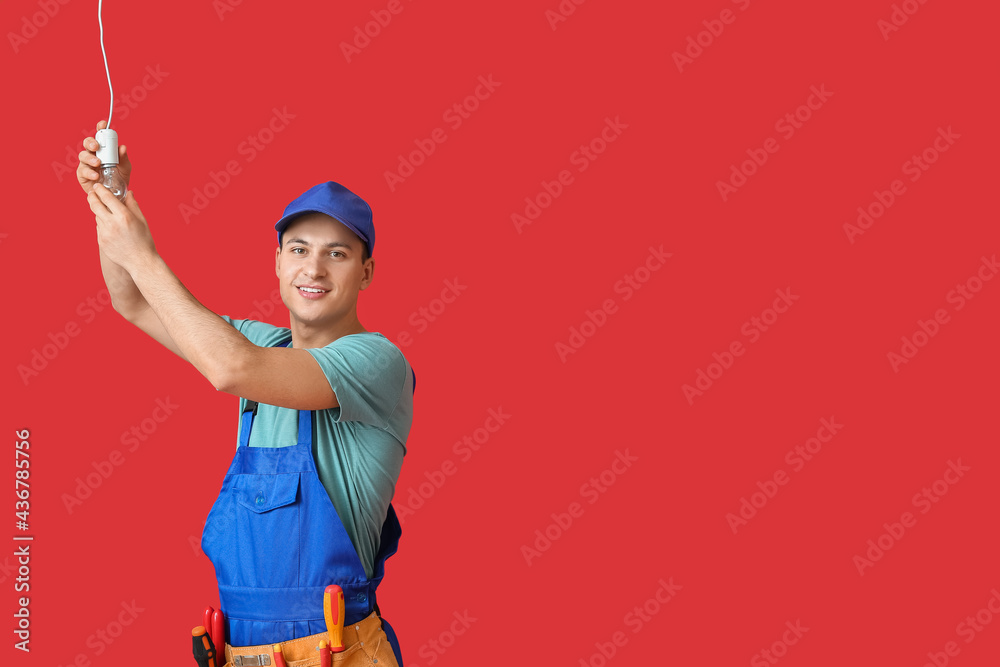 Young electrician screwing light bulb on color background