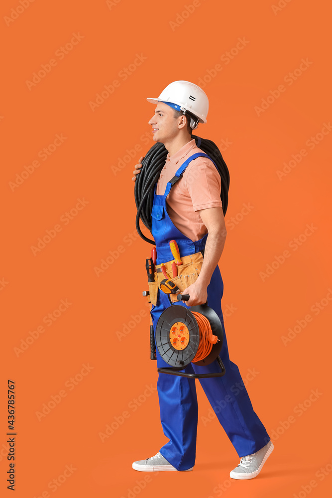 Young electrician with cables on color background