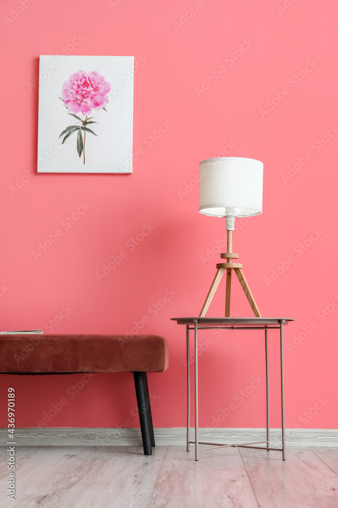 Table with lamp and ottoman near color wall