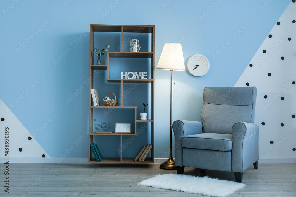 Glowing lamp with armchair and book shelf near color wall