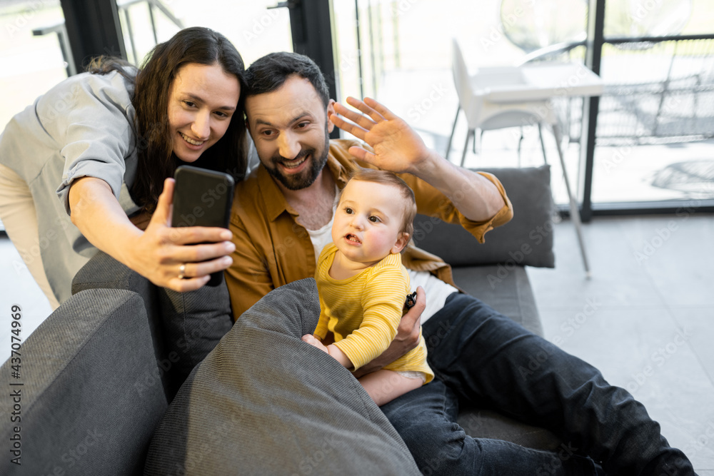 一个快乐的家庭，有一个一岁的男婴在家里通过电话进行视频通话。远程家庭的概念