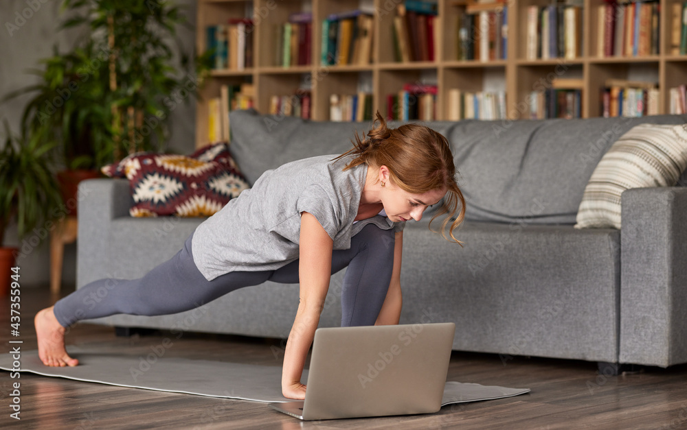 Young sporty woman yoga online with laptop in living room at home