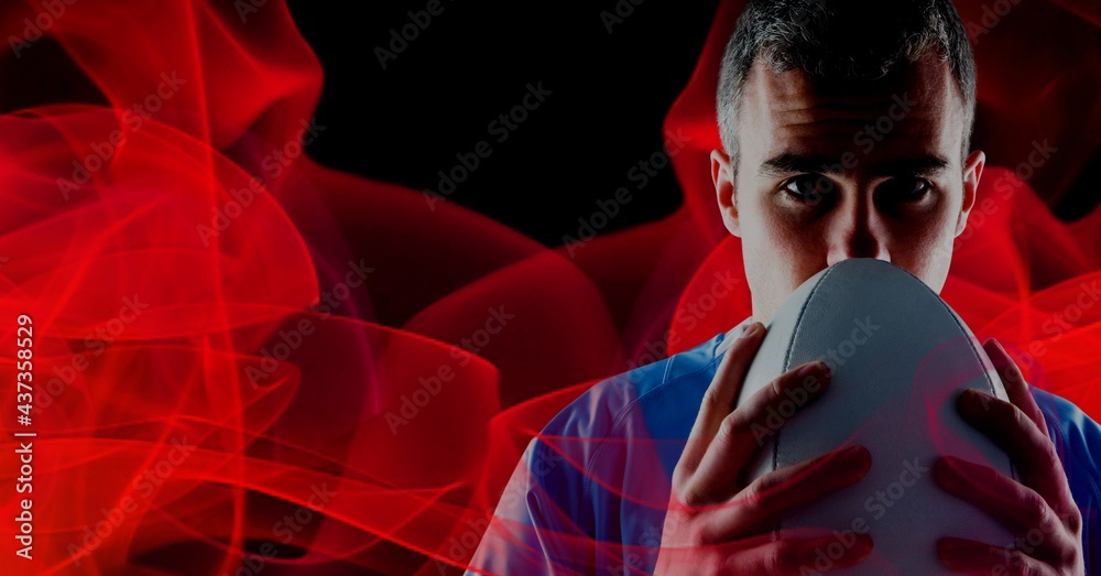 Compostion of caucasian rugby player holding ball on black background with red blur