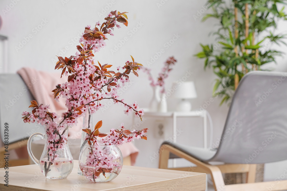 Vases with beautiful blossoming branches on table in room