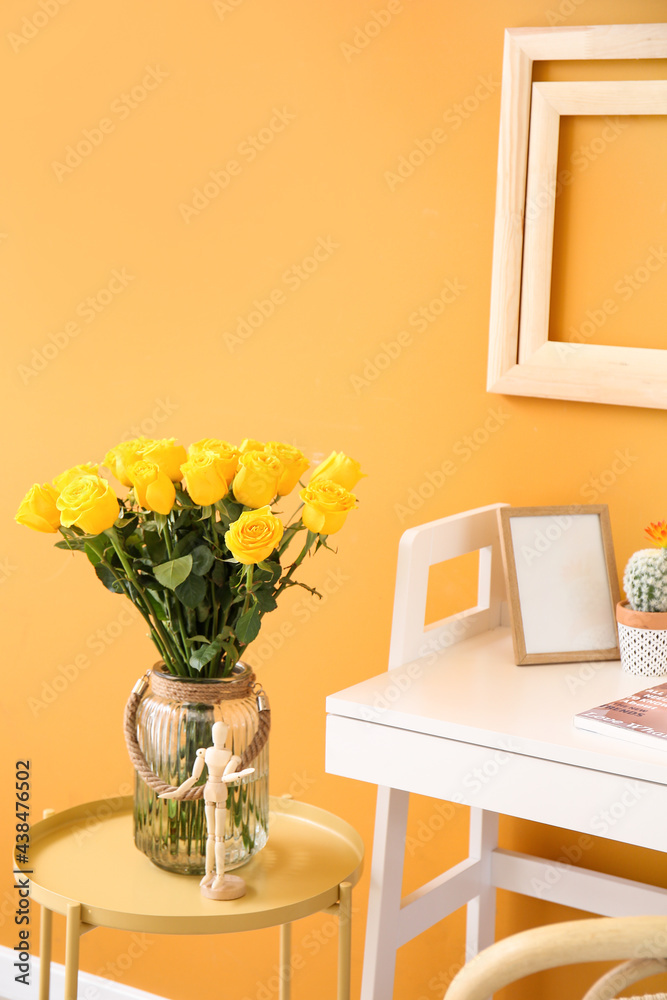 Vase with yellow roses on table near color wall
