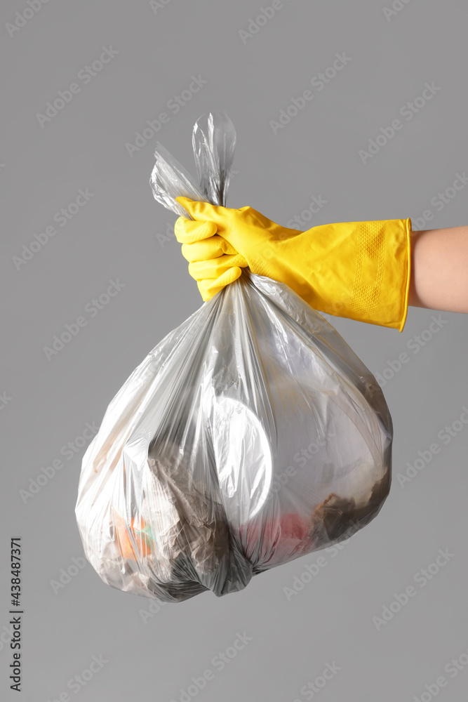Woman holding bag with garbage on grey background, closeup