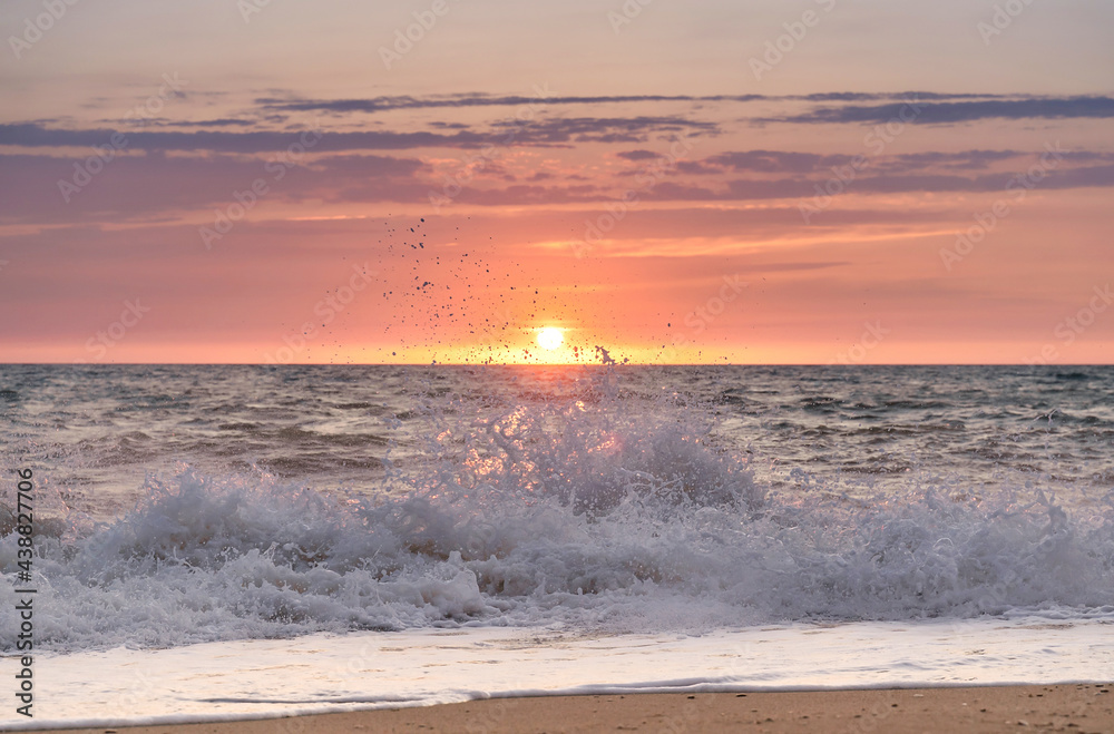 Green blue sea splashing waves backlit by setting sun in front of beautiful sunset sky background. T