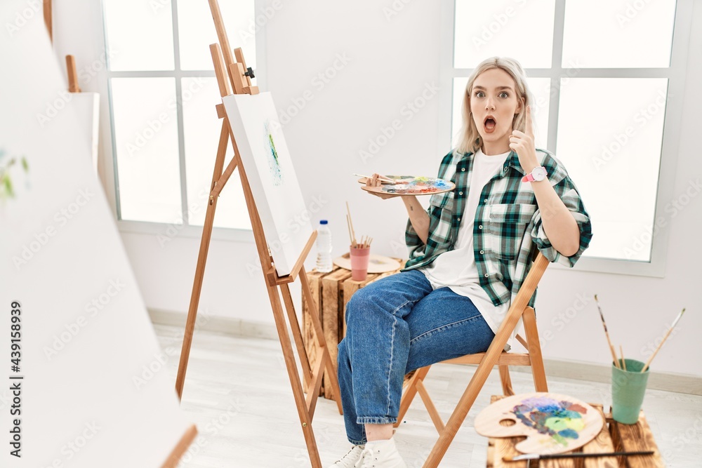 年轻的艺术家，一位在艺术工作室画布上作画的女性，用成功的想法指指点点。退出